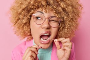 curly-haired woman flossing her teeth with one eye closed