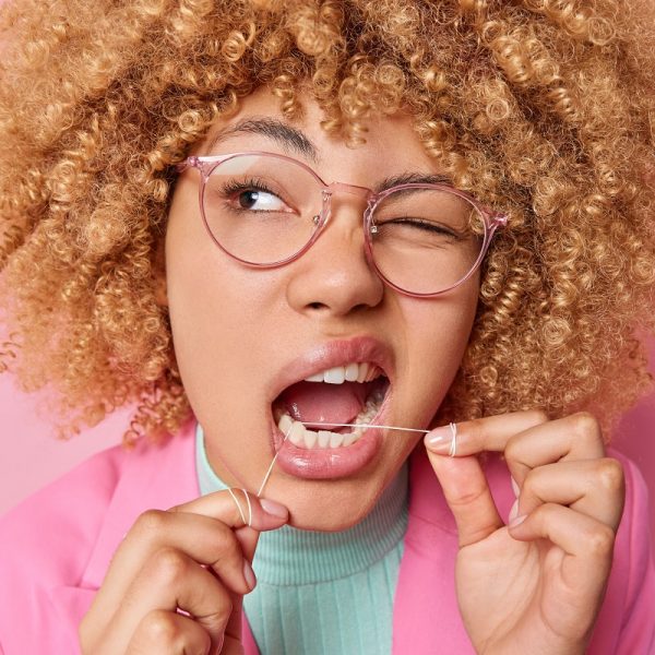 curly-haired woman flossing her teeth with one eye closed