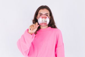 woman in a pink sweater holding a magnifying glass to her mouth, revealing irritated gums